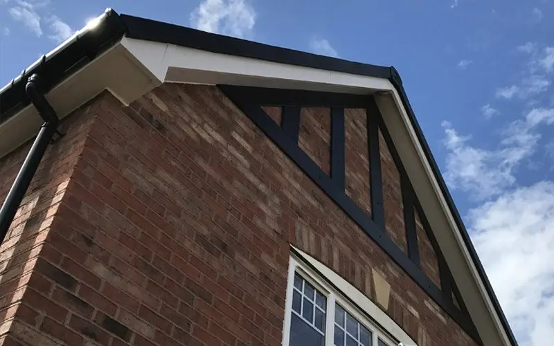 Top corner of a brick house showcasing black and white architectural detailing against a blue sky with clouds.