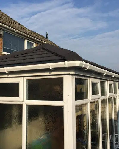 Glass conservatory roof with a sloped design, surrounded by a cloudy sky and residential buildings.