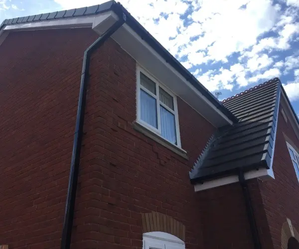 Two residential buildings with red brick exteriors, a white window, and a blue sky with scattered clouds.