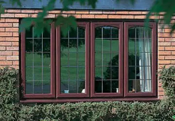 Window with multiple panes set in a brick wall, surrounded by greenery and a view of green grass outside.