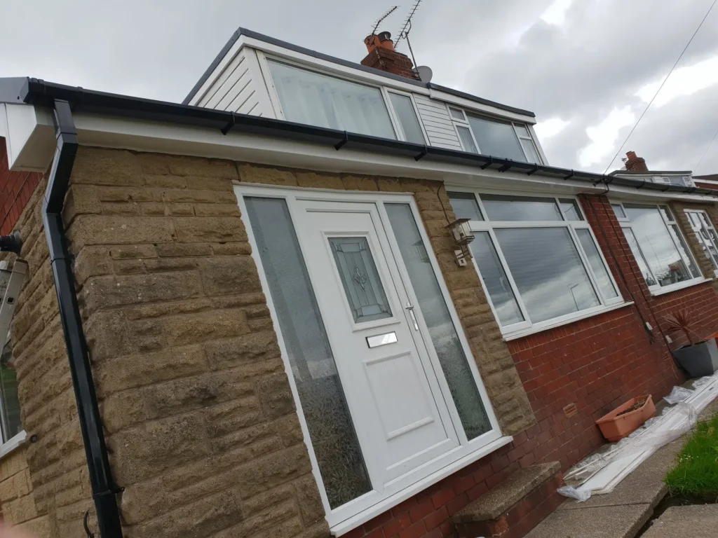 Residential home with stone and brick exterior, featuring a white front door and large windows under a cloudy sky.