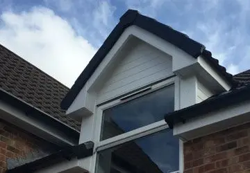 Corner of a house featuring a gable with a large window and a cloudy blue sky in the background.