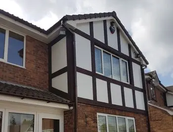 Two-story house with a combination of brown brick and white stucco, featuring multiple windows and a peaked roof.