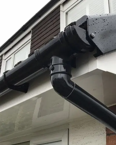 Black rain gutter system attached to the edge of a building with rainwater droplets visible.