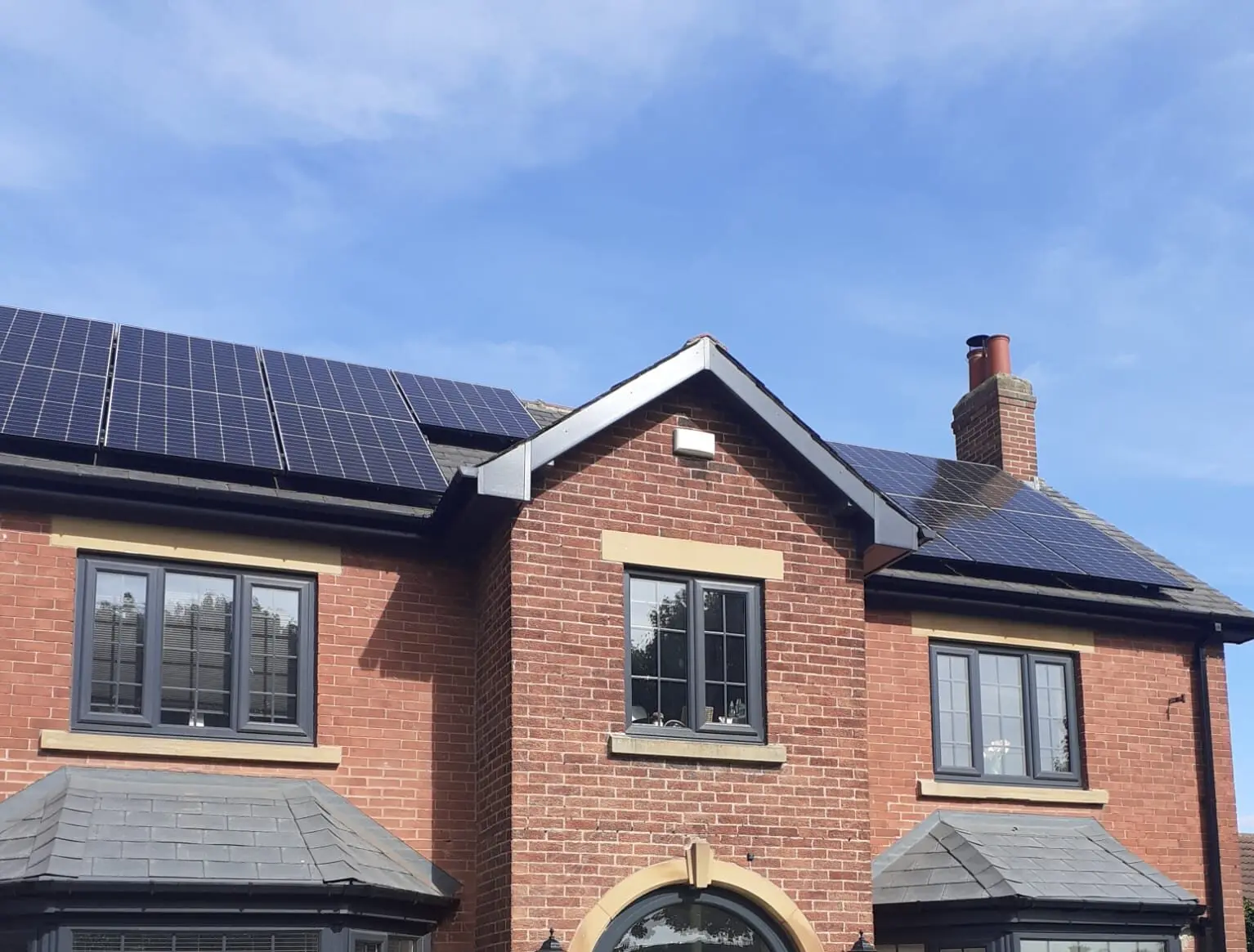 House with brick exterior featuring solar panels on the roof under a blue sky.