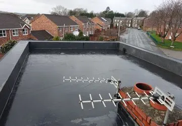 Flat roof with a TV antenna and chimney, overlooking residential houses and a road on a cloudy day.