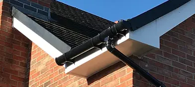 Gutter attached to a house with a brick wall and roof under a clear blue sky.