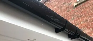 Black rain gutter attached to a white eave, with brick wall in the background.
