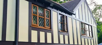 Tudor-style house with timber framing, multiple windows, and a shaded area in the garden.