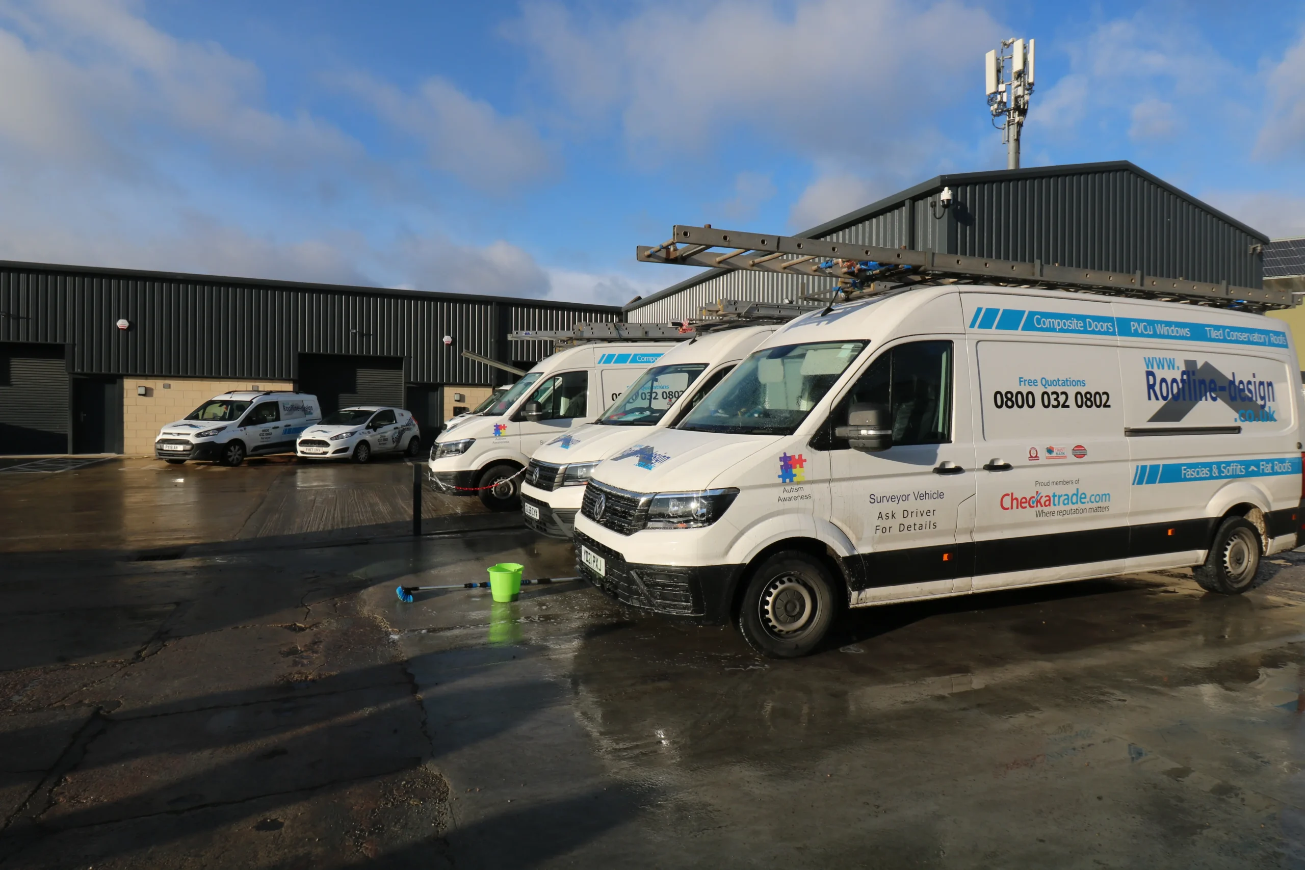 Three vans parked in front of a warehouse, with a green bucket and tools on the ground.