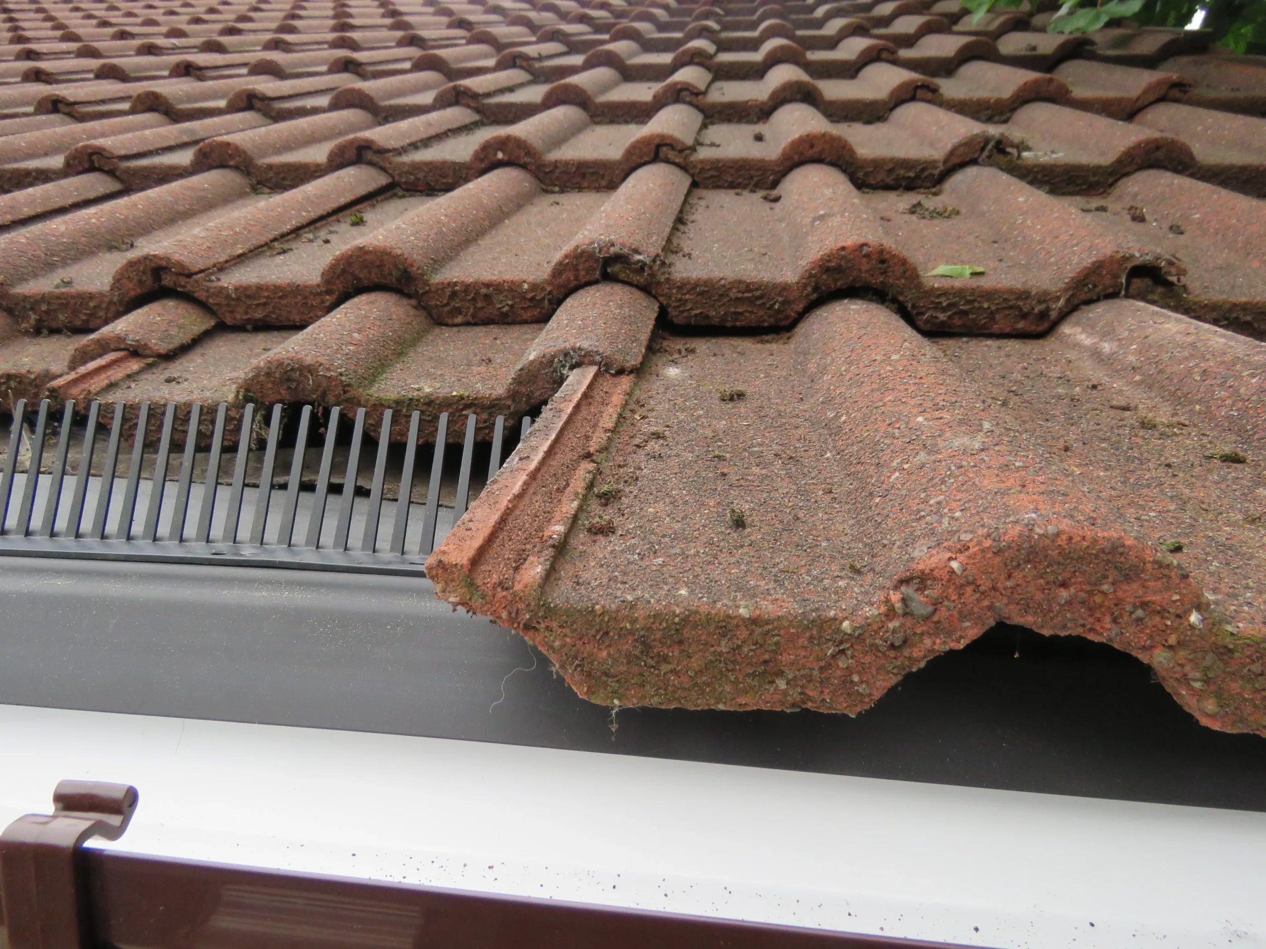 Damaged terracotta roof tiles with moss, partially covering a black gutter.