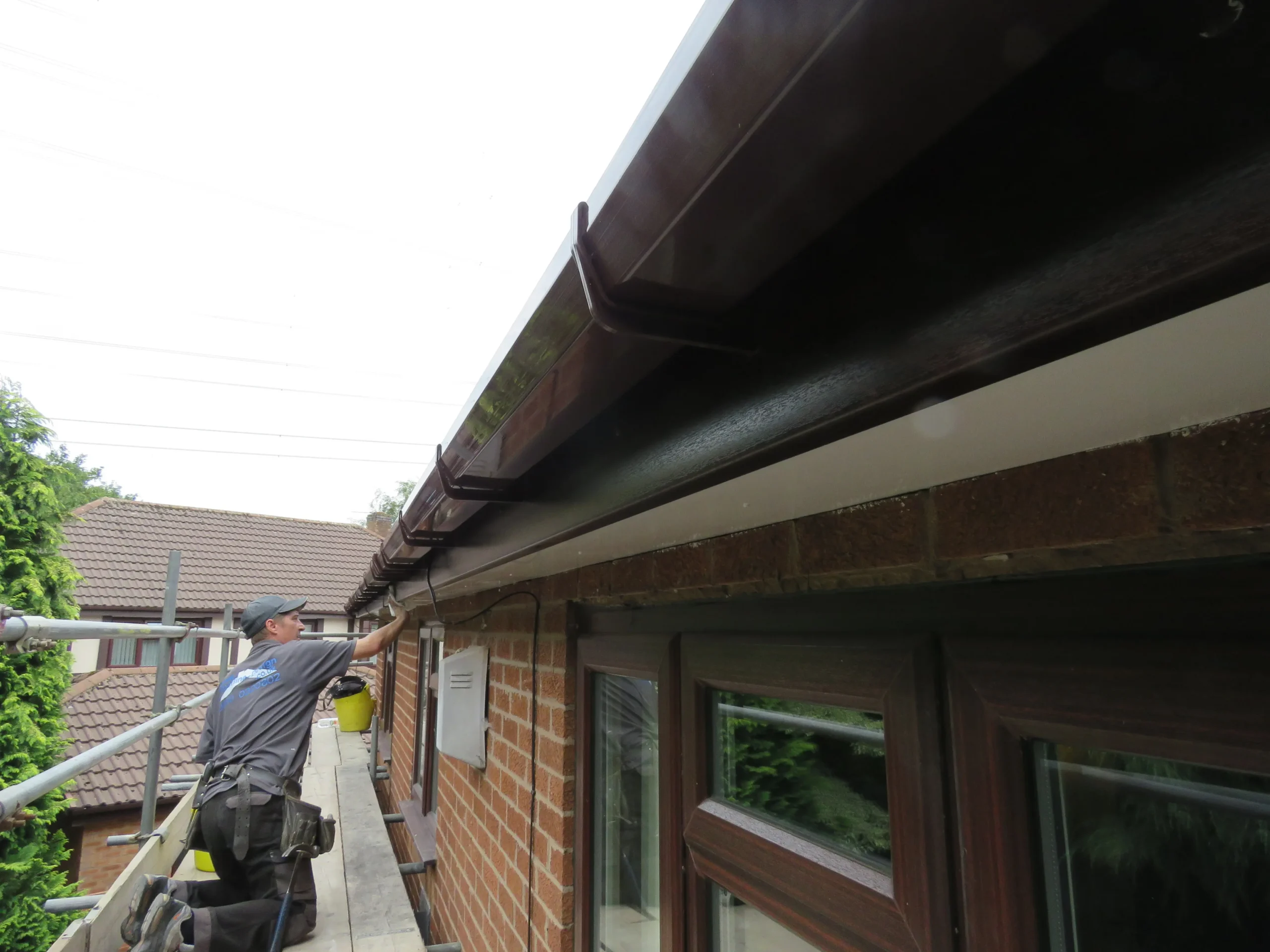 Worker kneeling on a scaffold, applying finishing touches to the gutter of a brick house.