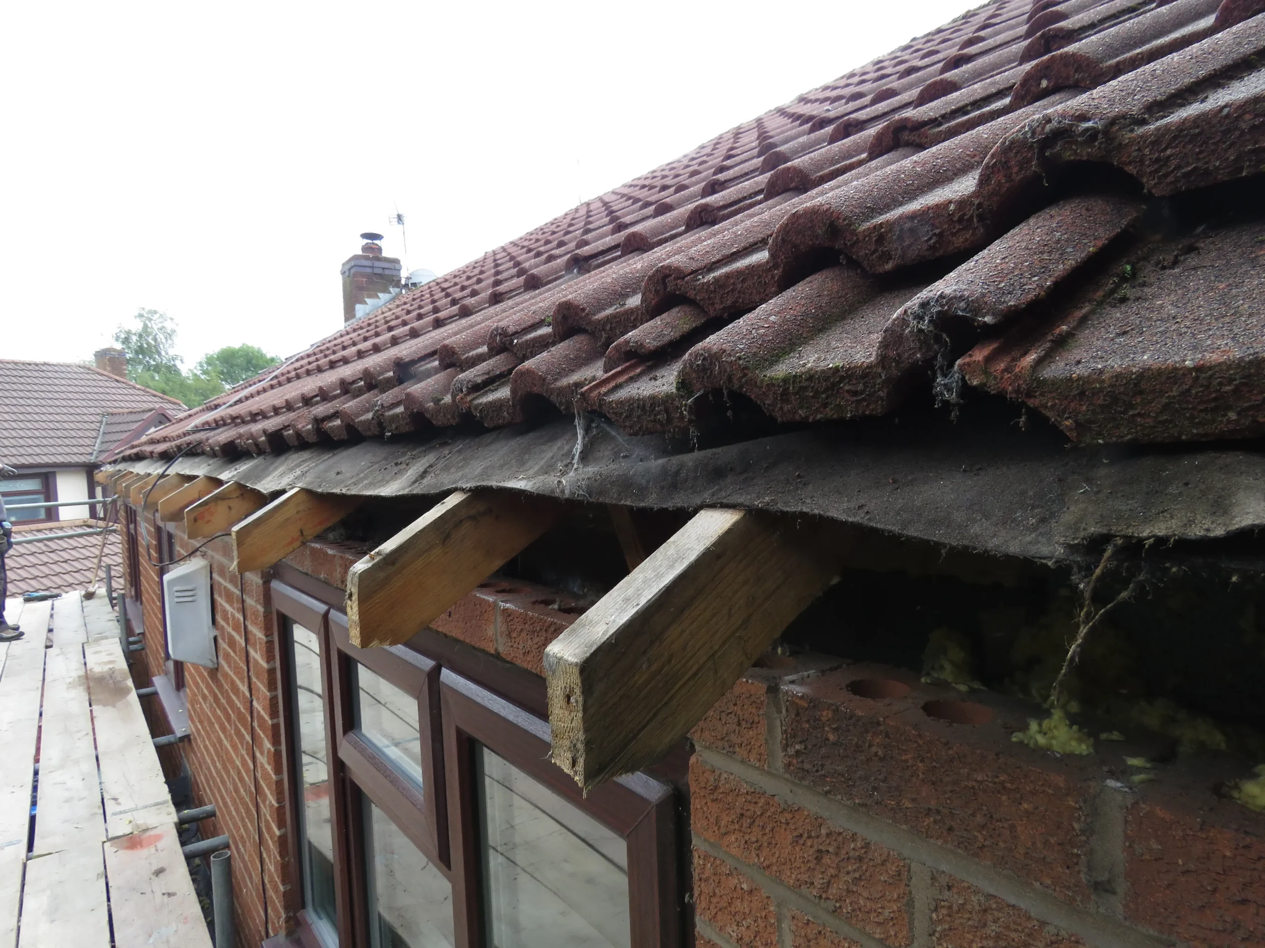 Roof with red tiles, exposed wooden beams, and a gap showing insulation beneath the eaves.