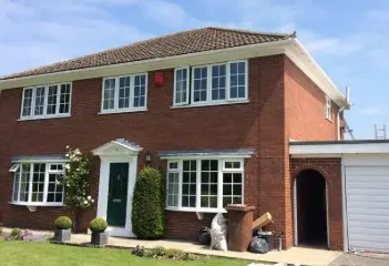 Two-story red brick house with white windows, green door, and garage; shrubs and decorative plants in front yard.