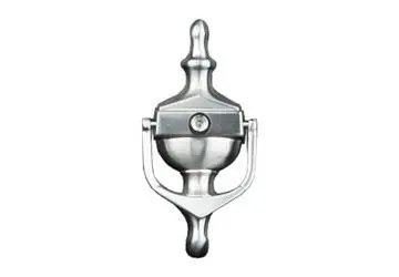 Metal door knocker with a round center and decorative finial on top, mounted on a flat surface.