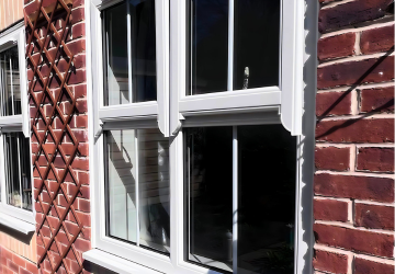 Gray-framed windows on a brick wall with a trellis structure alongside.