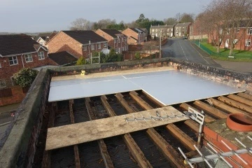 Roof with exposed beams and a partially installed flat roof covering, overlooking a residential street.