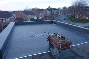 Flat rooftop with a chimney and an antenna, overlooking residential buildings and a road.