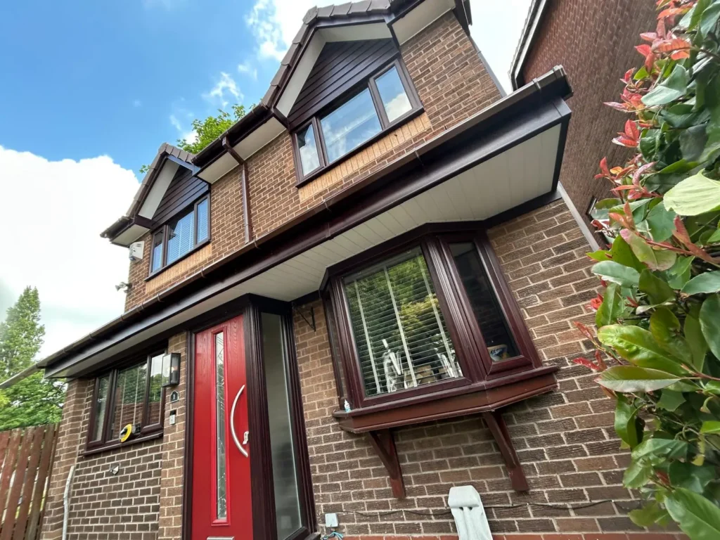 Two-story brick house with a red front door, large windows, and leafy plants nearby under a blue sky.