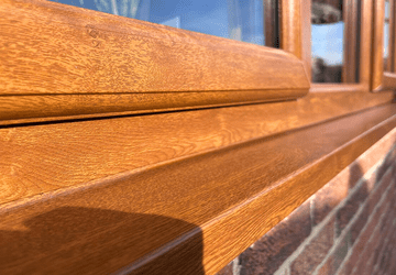 Wooden window sill with a smooth finish and sunlight casting a shadow on a brick wall.