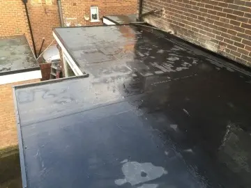 Flat roof surface with a black waterproof coating, showing some water puddles from recent rain.