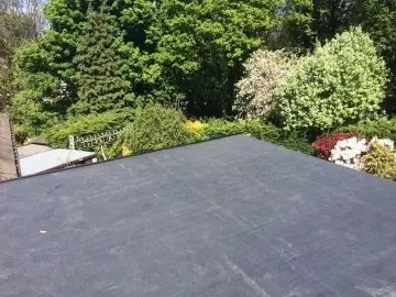 Flat rooftop with greenery including various trees and flowering plants in the background.