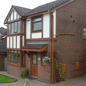 Two-story brick house with white panels, brown trim, front door, and landscaped pathway.