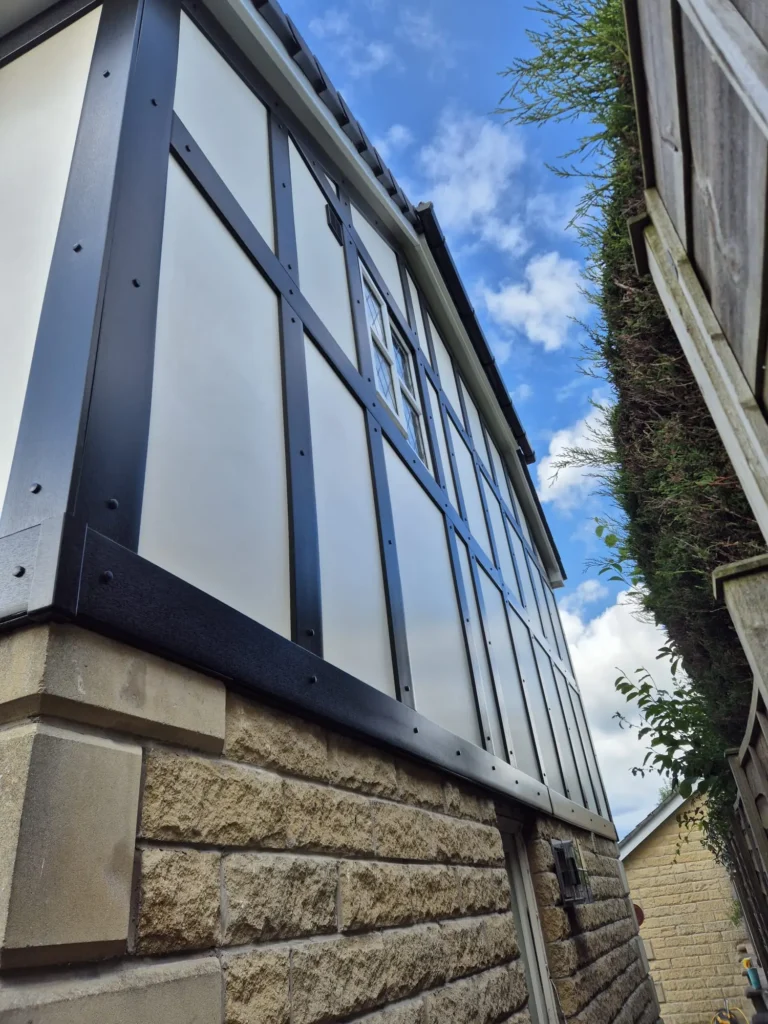 Two-story building with black framing and stone base, captured from a narrow side alley under a cloudy sky.