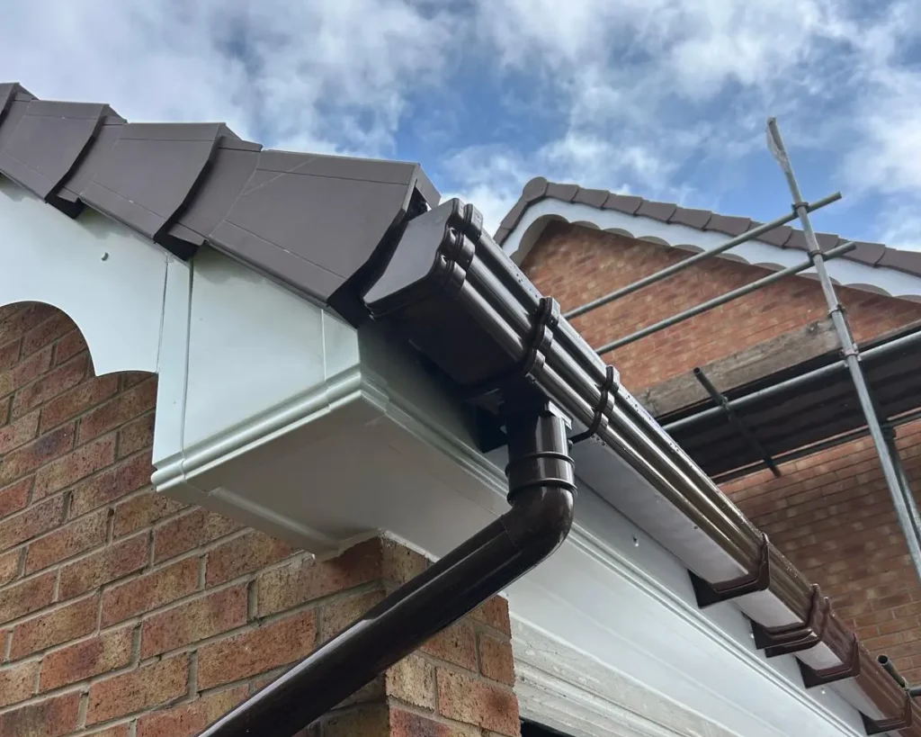 Gutter system installed on the edge of a roof with brown tiles and scaffolding in the background.