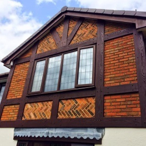 House exterior featuring brown timber framing and a brick facade with a large window under a cloudy sky.