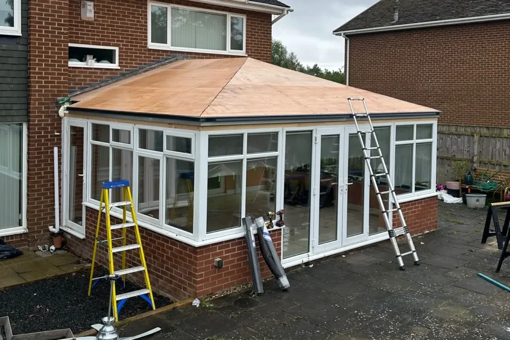 Conservatory with a wooden roof under construction, featuring ladders and tools on a patio.