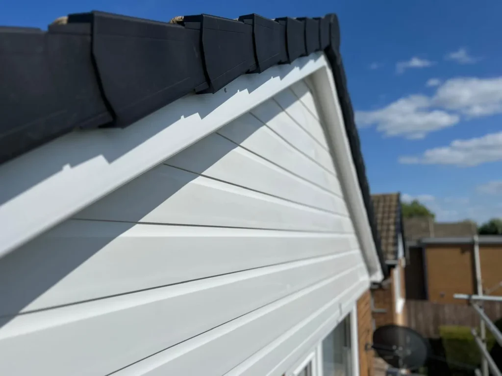 White house siding and black roofline against a blue sky with clouds.